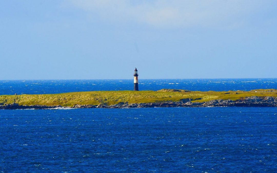 Costa de las Islas Malvinas con un faro sobre un promontorio de pastizal y el mar del Atlántico Sur en primer plano